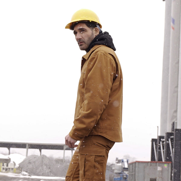 Man wearing a yellow hard hat and brown work jacket on a snowy day.